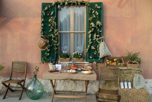 A rustic outdoor setting with a table set for a meal, a green window with shutters, and various food items and decorations. - Eco House San Michele (Latina)