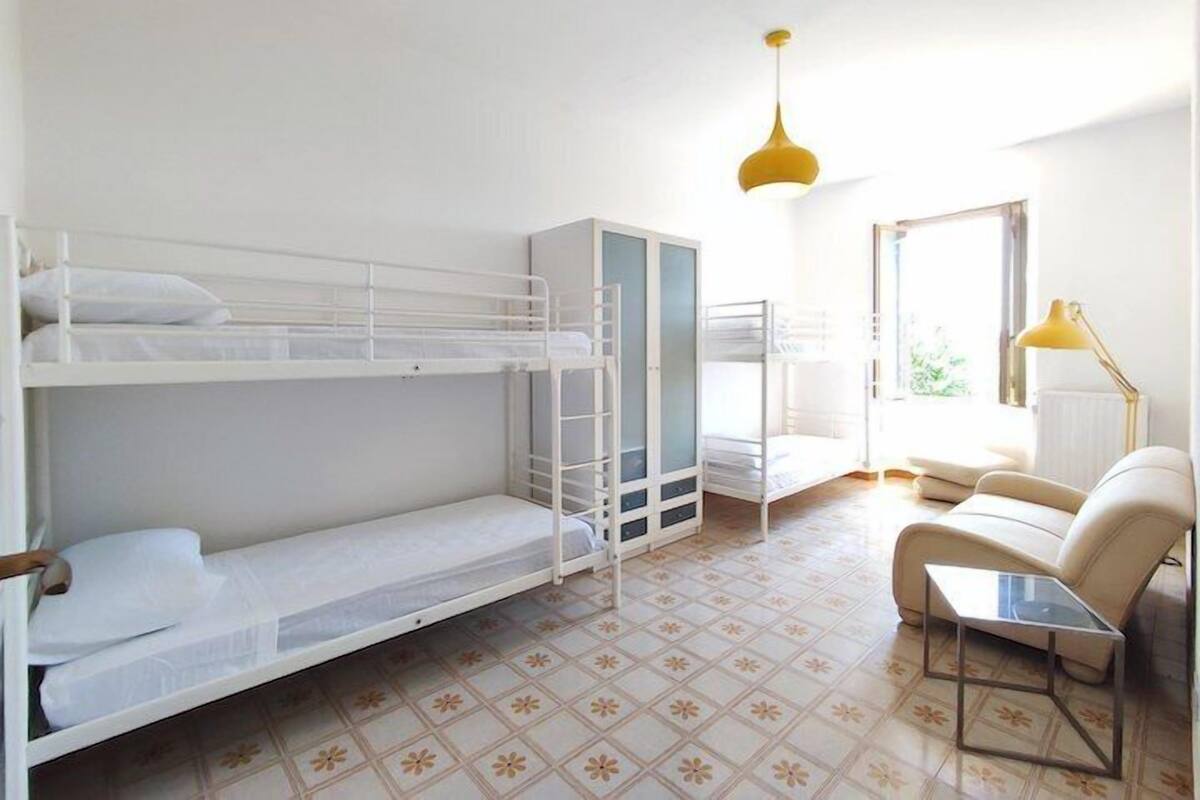 A room with bunk beds, a wardrobe, a sofa, a small table, and a hanging light fixture.
