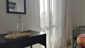 A room with a table holding a bottle, glasses, and a book. A metal bed frame is visible in the corner. - Eco House San Michele (Latina)