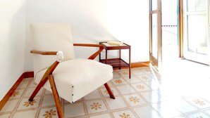 A room with a white air conditioner, a wooden chair, a small wooden table, and a tiled floor with a floral pattern. - Eco House San Michele (Latina)