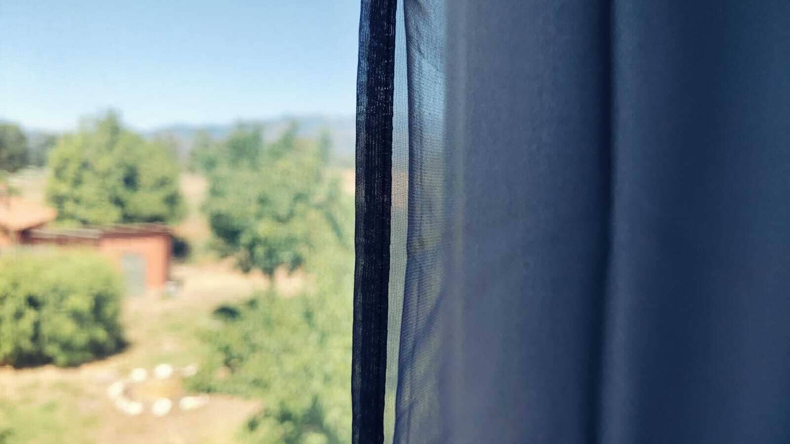 Una ventana con vistas a un paisaje rural, con árboles y un edificio pequeño.