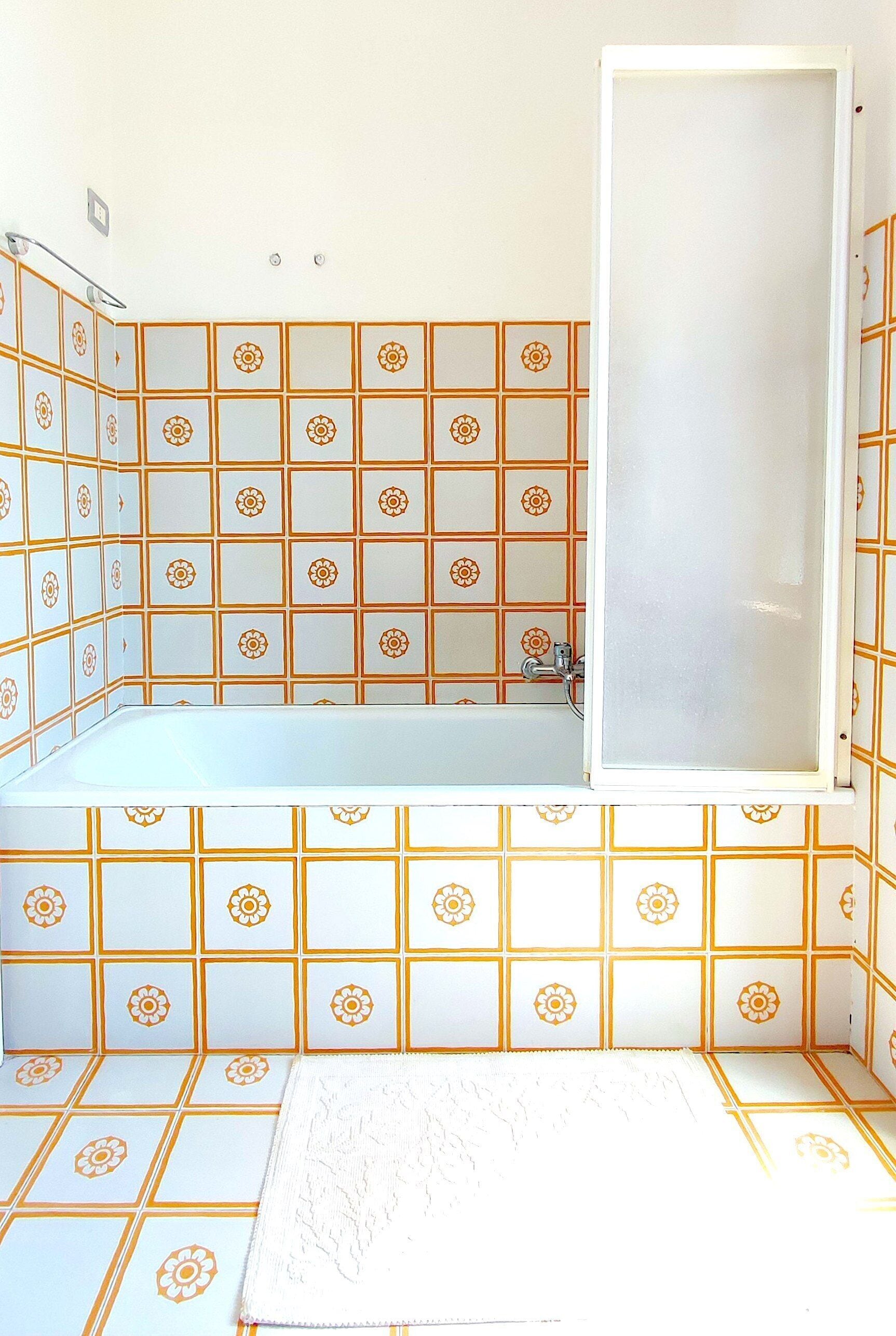 Un bagno con vasca, doccia e servizi igienici. Le pareti sono rivestite con un motivo geometrico.