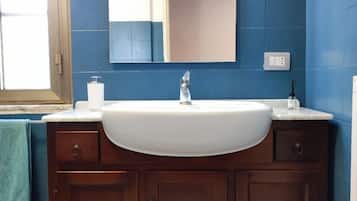 Een badkamer met een wit wastafelmeubel, houten kast, blauwe tegels, een spiegel en een handdoekhouder.