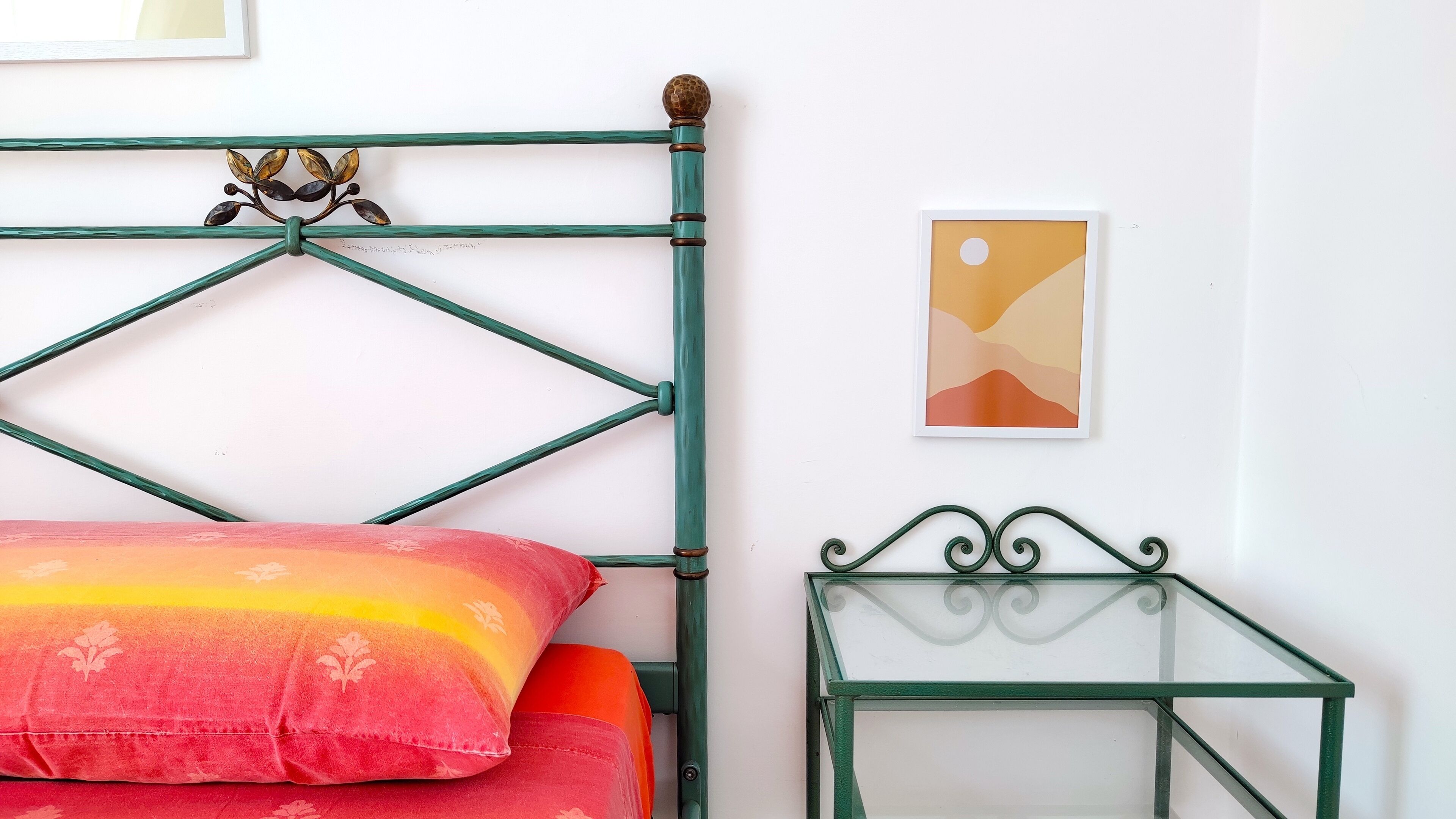 Un letto con struttura in metallo verde, una pianta decorativa e un'opera d'arte incorniciata al muro.