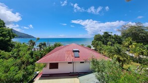 A house with a red roof, surrounded by lush greenery and a view of the ocean. - Modern and Private - 1min from the Beach! (Beau Vallon)