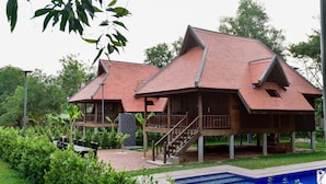 A two-story wooden house with a red-tiled roof, a swimming pool, and a garden area with greenery and outdoor seating. - Angkor Heart Bungalow- Private Pool (Siem Reap)
