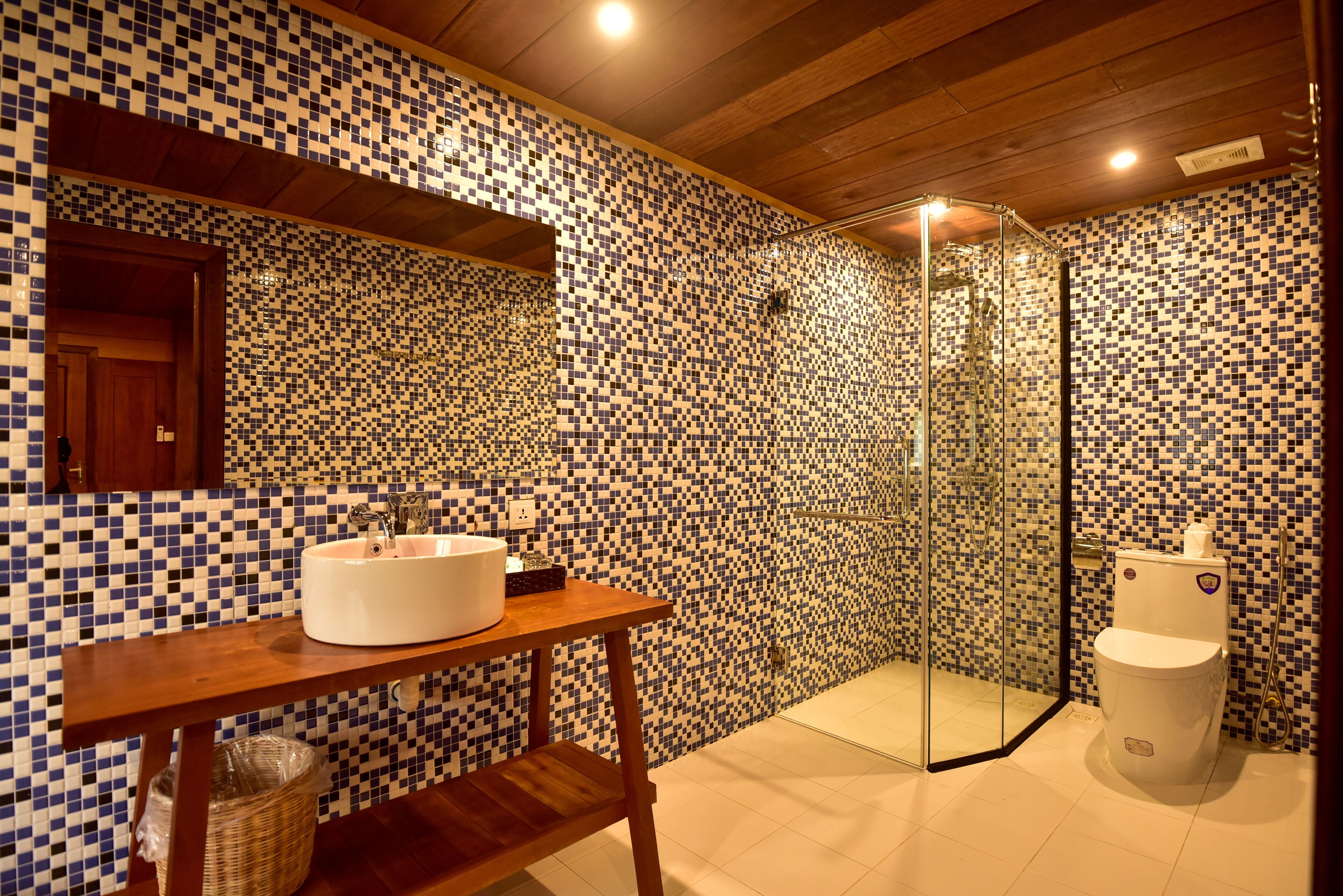 Een badkamer met mozaïektegelwanden, een houten wastafelmeubel met een wastafel, een glazen douchecabine en een toilet.