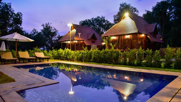 A poolside area with lounge chairs and a swimming pool, surrounded by lush greenery and wooden buildings with warm lighting. - Angkor Heart Bungalow- Private Pool (Siem Reap)