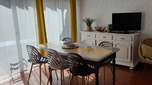 A dining area with a table, chairs, a television on a cabinet, and a window with curtains.