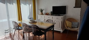 A dining area with a table, chairs, a television on a cabinet, and a window with curtains.