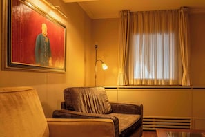 A room with a single armchair, a painting on the wall, a floor lamp, and a window with curtains. - Hotel Mitra (Ptuj)
