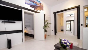 A modern hotel lobby with a flat-screen TV mounted on the wall, a reception desk with a vase of flowers, and a potted plant. - CAPRI Downtown Rooms (Mykonos)