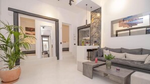 A modern living room with a grey sofa, a coffee table, and a potted plant. - CAPRI Downtown Rooms (Mykonos)