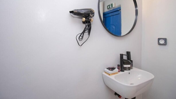 A bathroom with a white sink, a mirror, and a hairdryer mounted on the wall. - CAPRI Downtown Rooms (Mykonos)