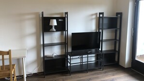 Une pièce d’angle avec un bureau, un meuble noir pour la télévision et une lampe.