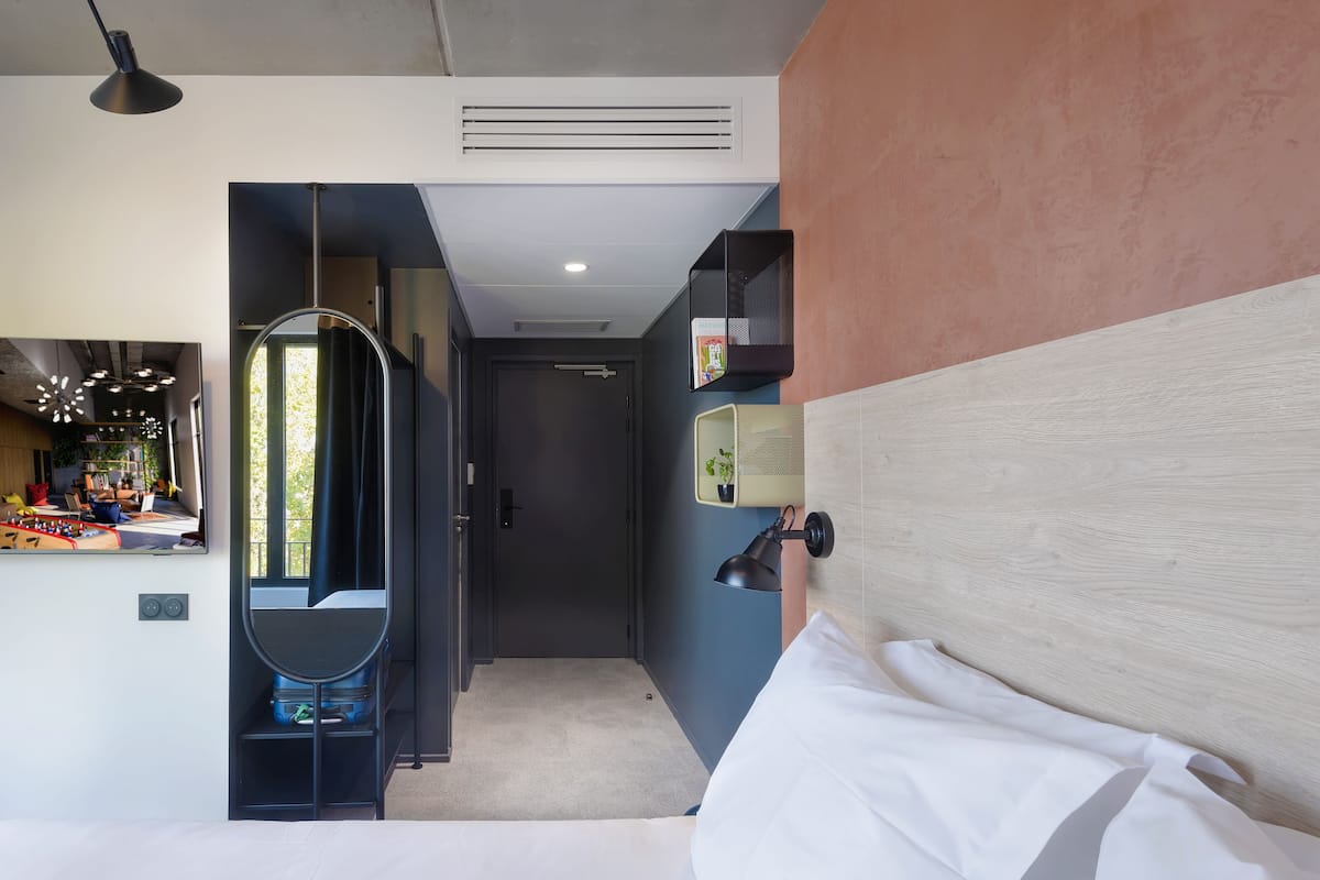 A modern hotel room with a bed, a desk, and a view of the outside.