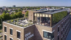 A modern building with the name "QUAI CENTRAL" on its facade, featuring a rooftop terrace with outdoor seating and a glass facade on the upper level. - Quai Central (Tourcoing)
