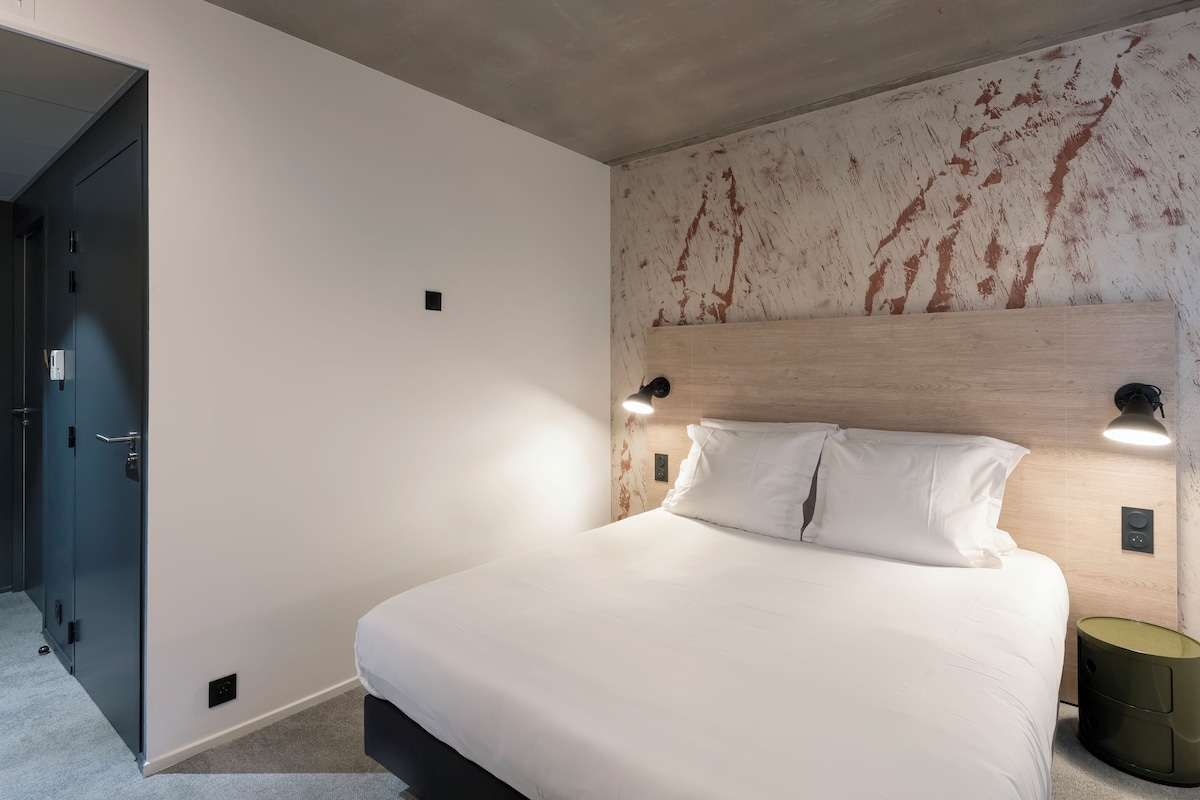 Une chambre moderne avec un grand lit, deux lampes de chevet et un mur au revêtement original.