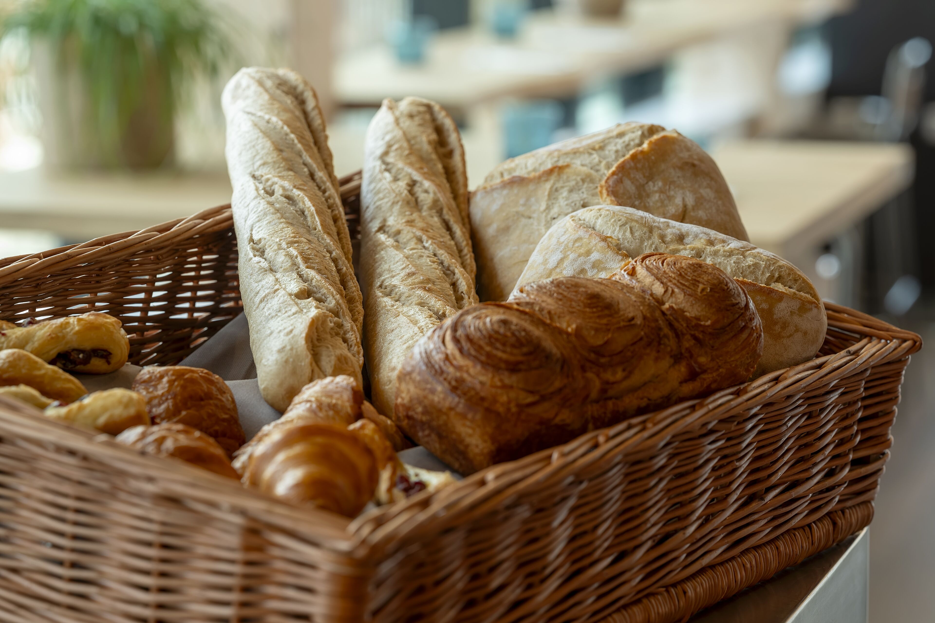 A wicker basket filled with various types of bread, including baguettes and croissants.