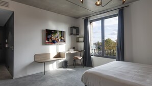 A modern hotel room with a large bed, a desk with a chair, a small seating area, a large window with curtains, and a painting on the wall. - Quai Central (Tourcoing)