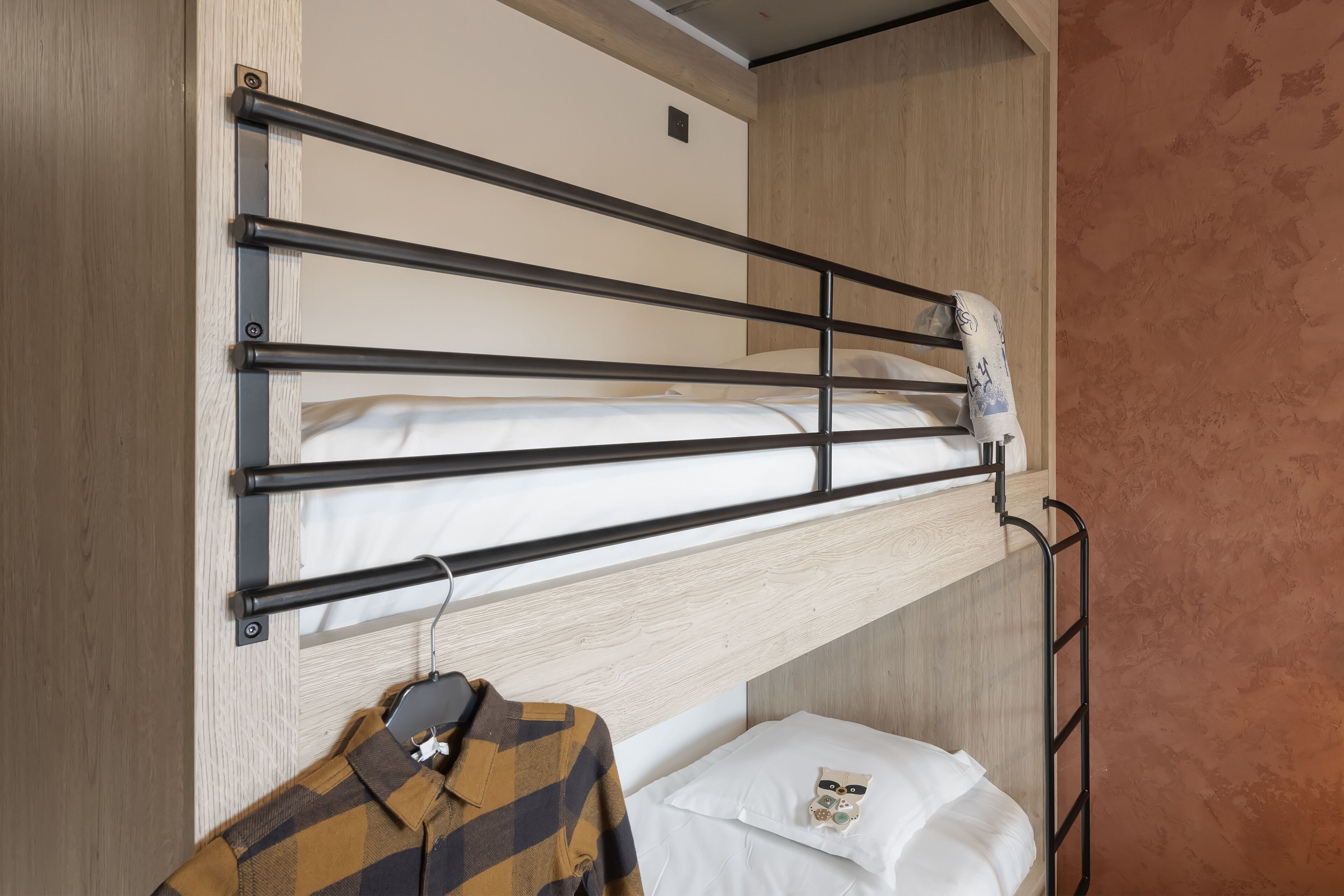 Una cama litera con escalera metálica, un perchero y un almohada decorada con un pequeño búho.
