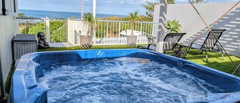 A hot tub with a view of the ocean, surrounded by a white pergola and outdoor furniture.