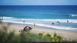 A beach with a lifeguard station and a small boat. - Beachfront, ocean views, private rooftop terrace with spa, pool, walk to beach (Marcoola)