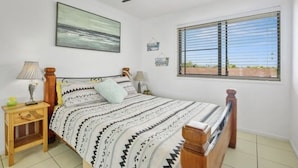A bedroom with a bed, a ceiling fan, a window with blinds, and a painting on the wall. - Beachfront, ocean views, private rooftop terrace with spa, pool, walk to beach (Marcoola)