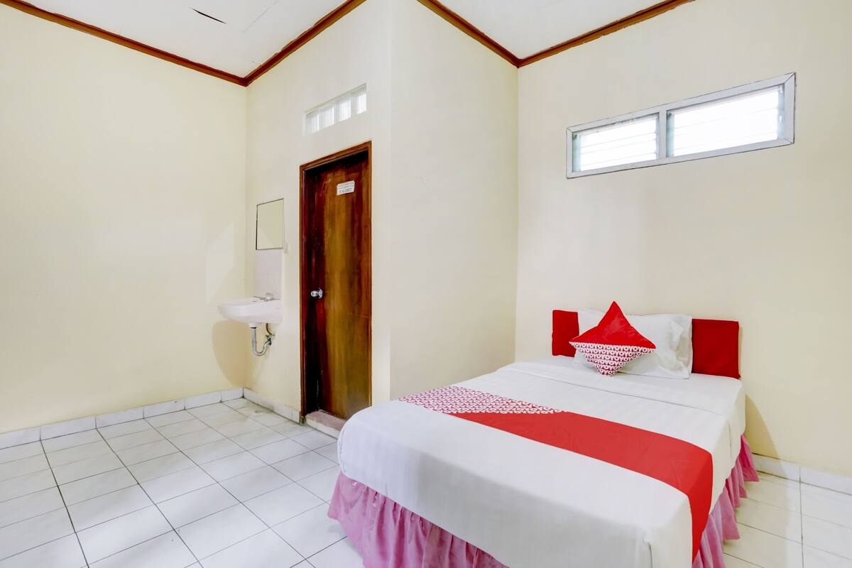 Un dormitorio con cama, ventana, puerta y lavabo.