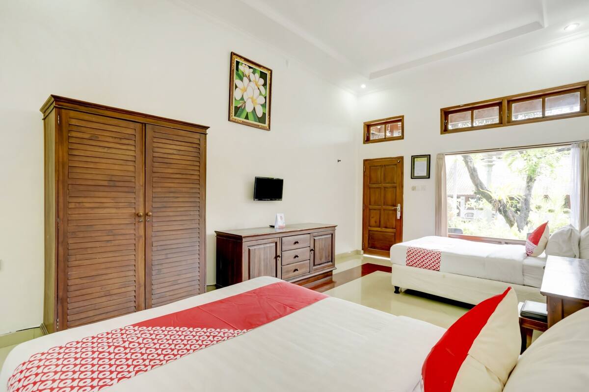 Habitación de hotel con dos camas, un armario, un televisor y una ventana con vista a áreas verdes.