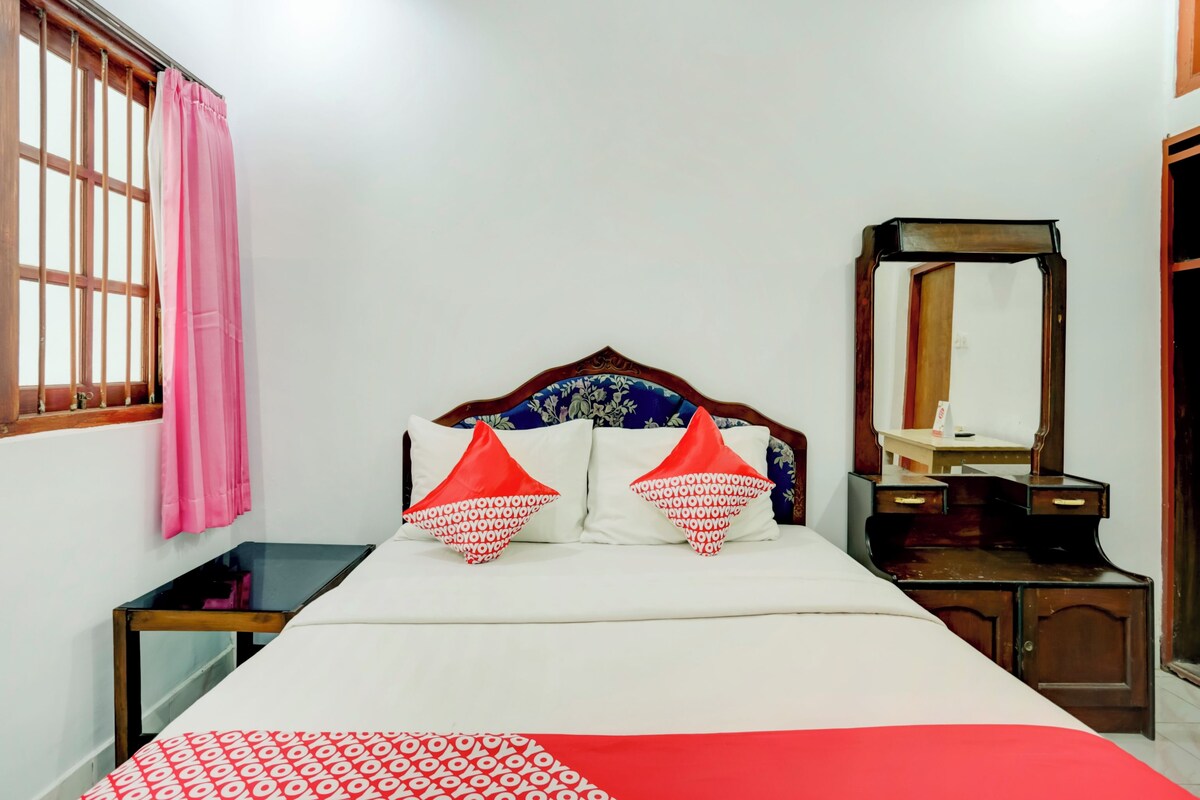 A bedroom with a bed, a bedside table, a mirror, and a window with curtains.