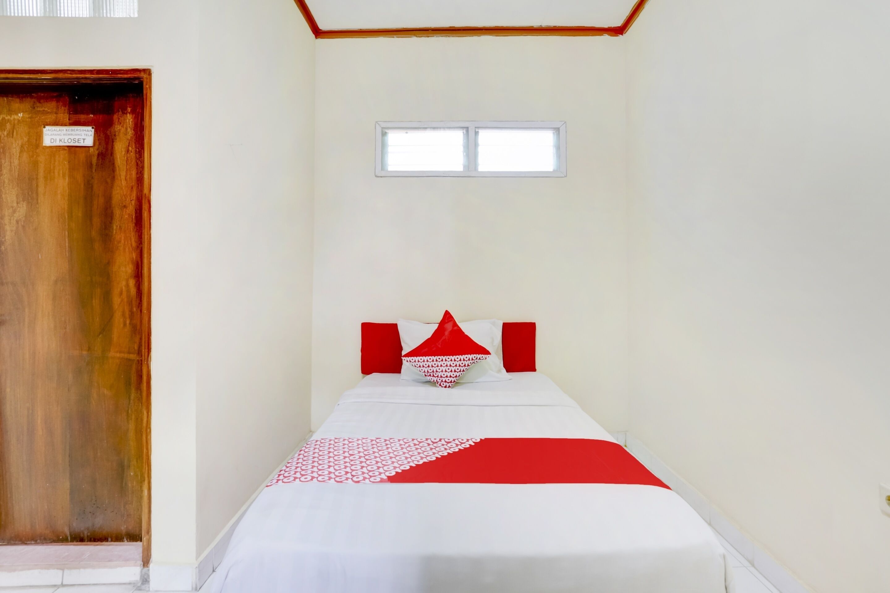 A small, simple room with a single bed, a window, and a wooden door.