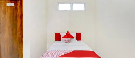 Una habitación pequeña y sencilla con una cama individual, una ventana y una puerta de madera.