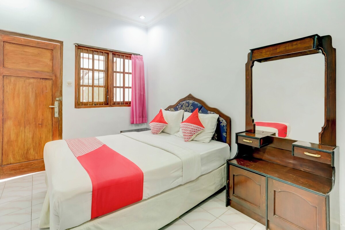 A bedroom with a bed, a wooden wardrobe, a mirror, a window with curtains, and a door.