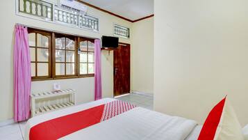Un dormitorio con cama, televisor montado en la pared, ventana con cortinas y puerta.