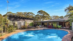 Une piscine avec des chaises longues, un patio couvert et un bâtiment doté d’un toit en tuiles.