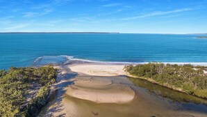 Un paysage côtier caractérisé par une plage de sable, une eau d’un bleu limpide et une végétation luxuriante.