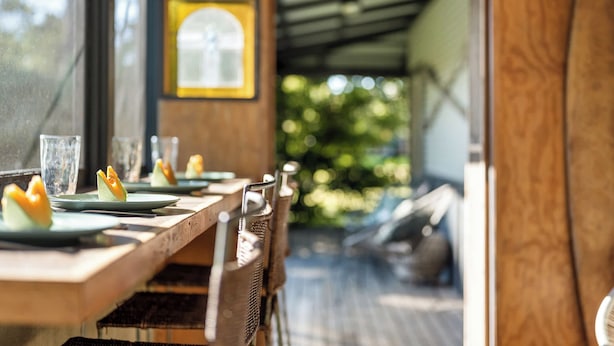 Un espace repas avec une longue table dressée pour le repas, des chaises et une vue sur la verdure à l’extérieur.