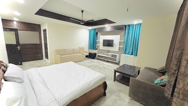 A hotel room with a large bed, a sofa, a TV mounted on the wall, and a ceiling fan. - Roomshala 074 Hotel Royal Inn (Noida)