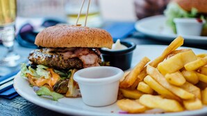 A plate with a burger, fries, and a small cup of sauce. - Roomshala 074 Hotel Royal Inn (Noida)