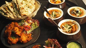 A table with various dishes including naan bread, a salad, and multiple bowls of curry. - Roomshala 074 Hotel Royal Inn (Noida)