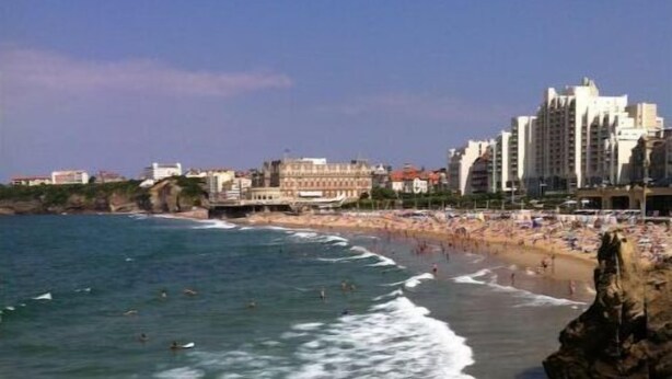 A coastal view with a beach, waves, and buildings in the background.