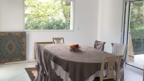 A dining area with a round table, chairs, a patterned rug, and a window with a view of greenery.