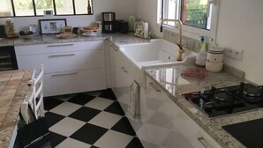 A kitchen with a black and white checkered floor, a gas stove, a sink, and a window with a view of greenery outside.