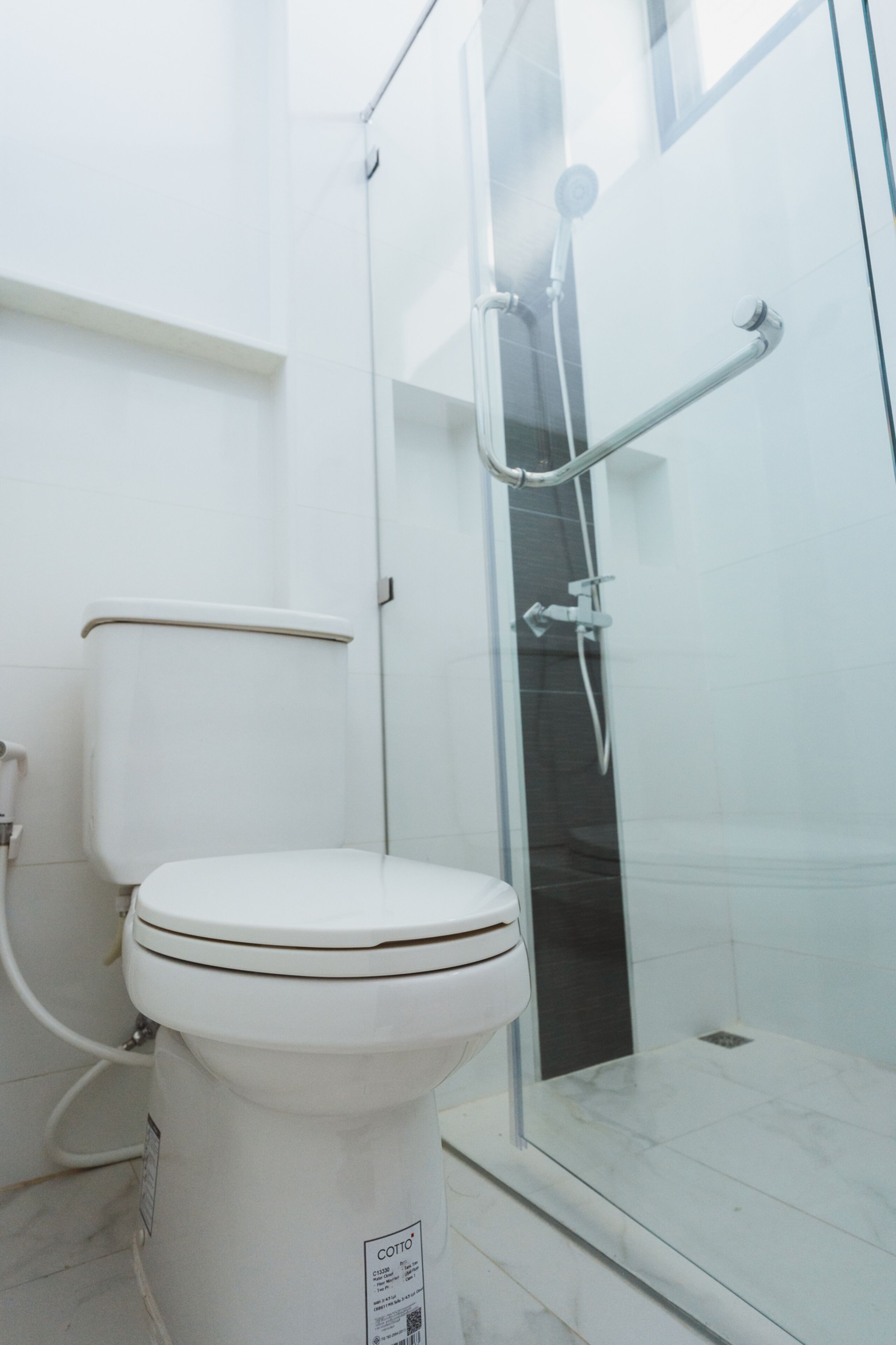 Een moderne badkamer met een toilet, een douchecabine van glas en een vloer betegeld met witte tegels.