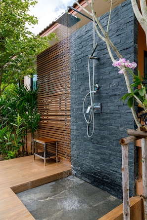 A modern outdoor shower area with a stone wall, wooden slats, and a bench.