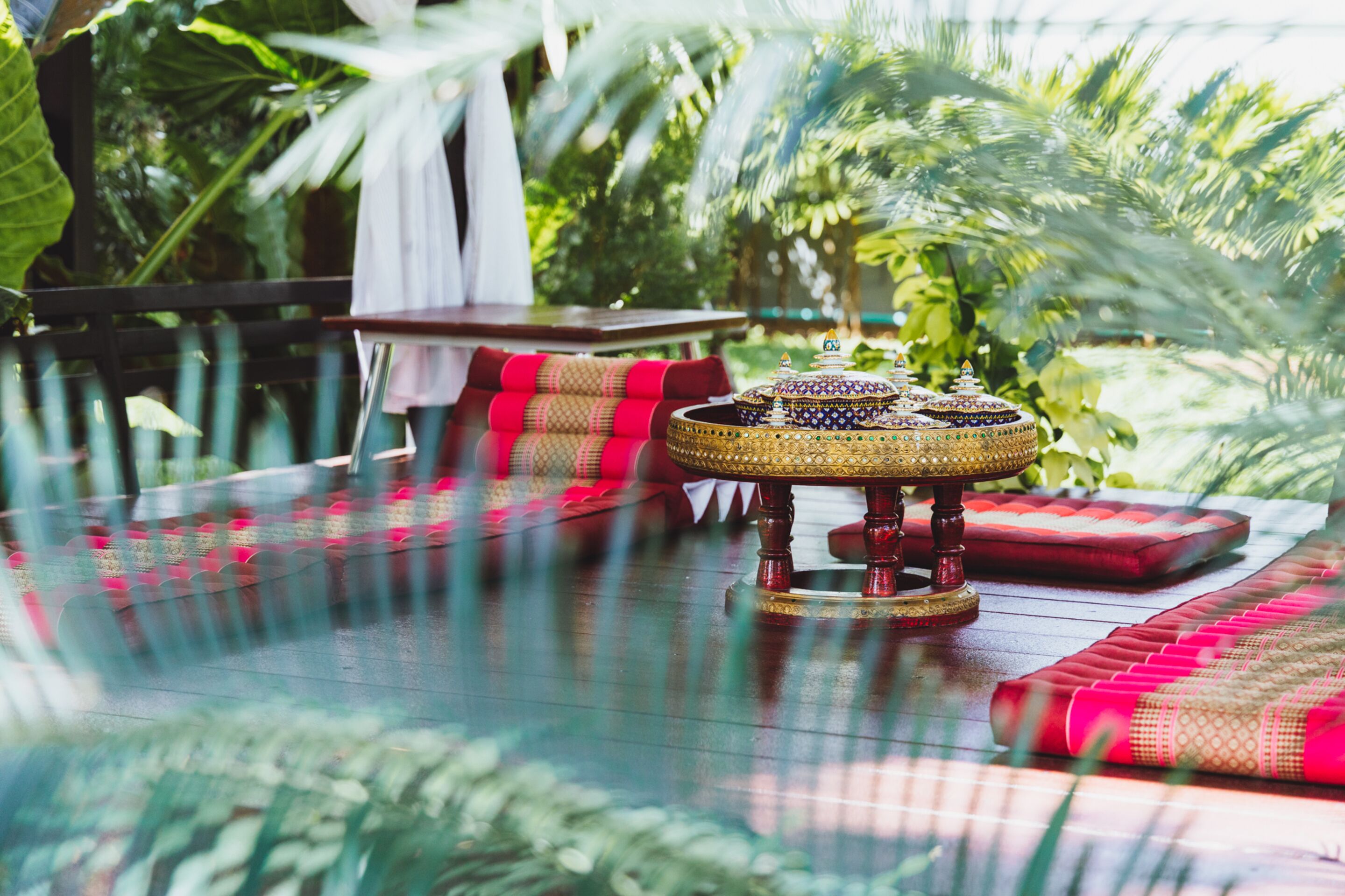 A glass table with a decorative brass centerpiece, red cushions, and a white cloth hanging on a metal railing.