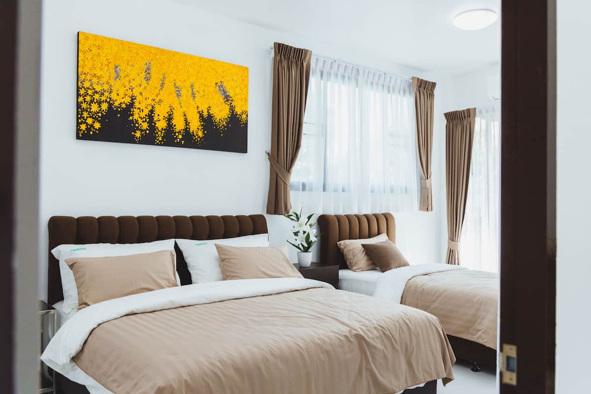 Een hotelkamer met twee bedden, een groot raam met gordijnen, een schilderij aan de muur en een potplant.