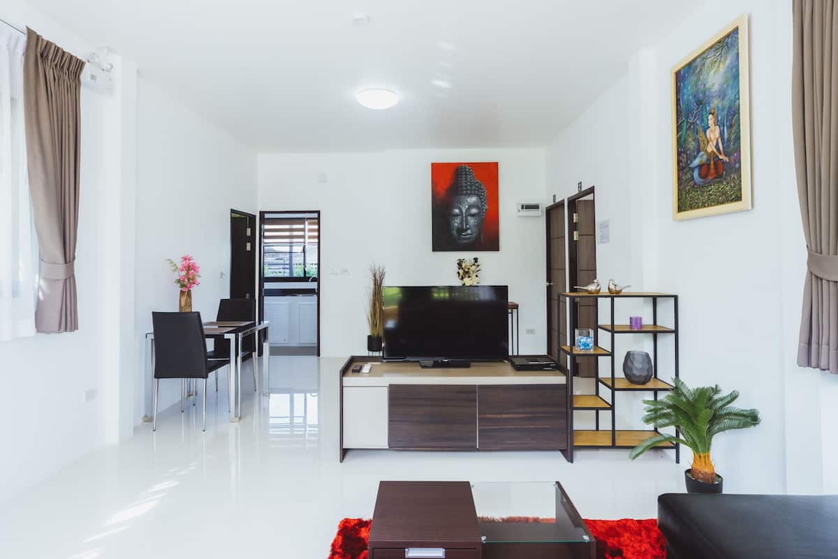Een moderne woonkamer met een flatscreen televisie, een eethoek met stoelen en een tafel, een boekenkast en een potplant.
