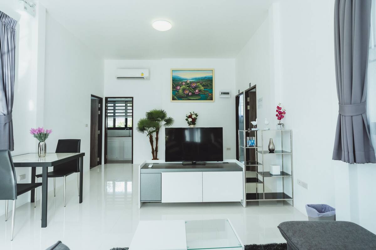 Een moderne woonkamer met een flatscreen televisie, een eettafel met stoelen, een glazen salontafel en een bank.